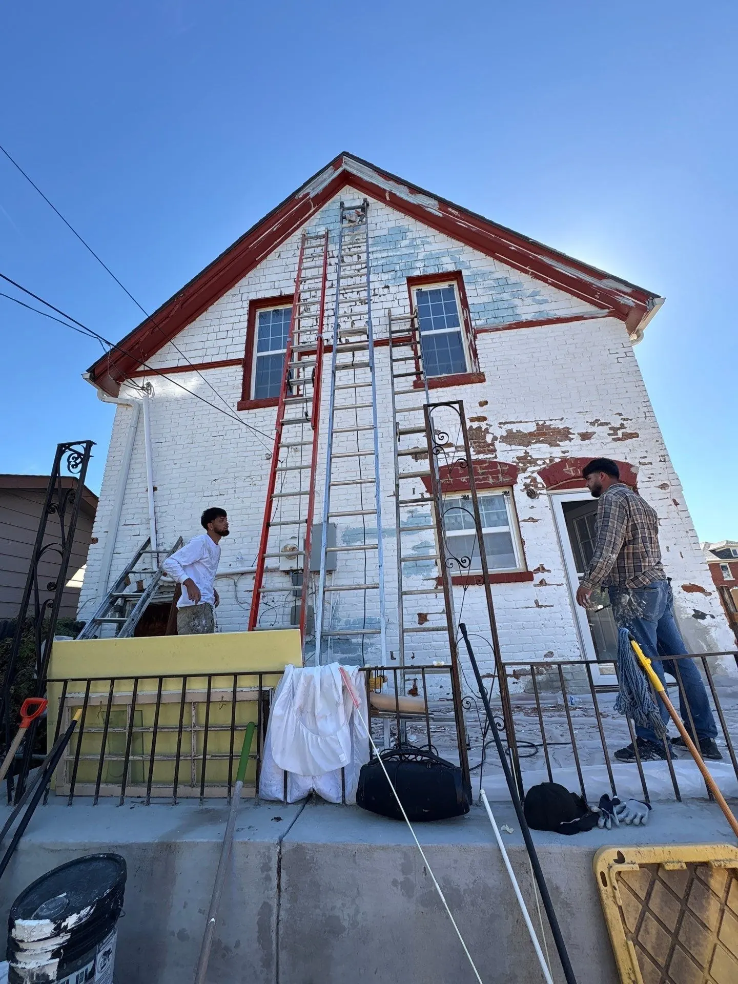 Kind Home Painting crew on ladders beside a side wall of painted brick with heavy peeling paint on a historic Denver Victorian