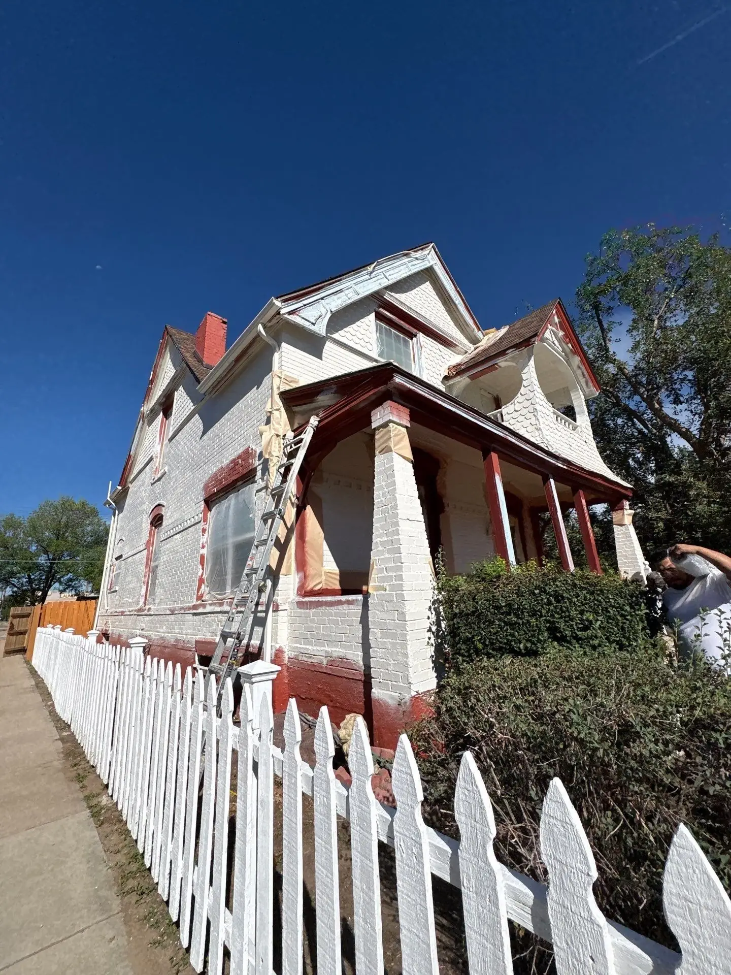 Masked windows and freshly primed painted brick on a Denver Victorian mid-project, with a ladder against the porch