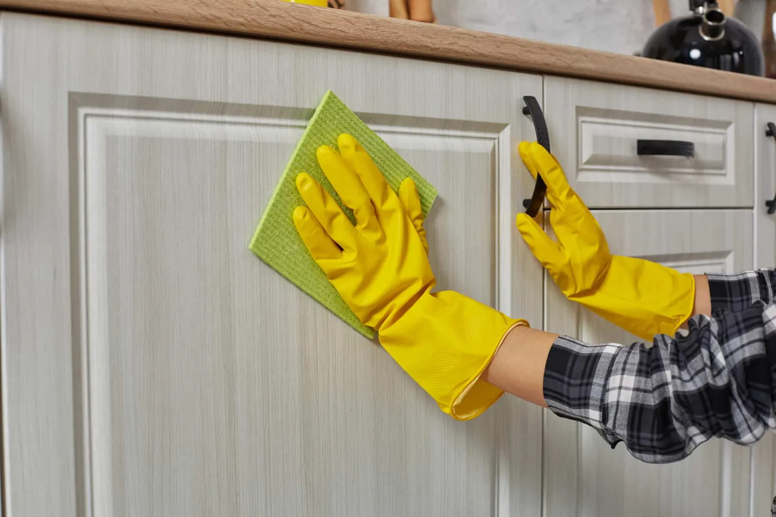 A kitchen cabinet interior being cleaned with a cloth and spray bottle